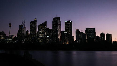 Illuminated buildings by river against sky in city at night