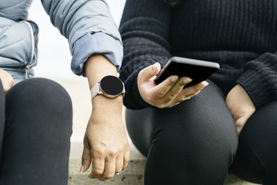 Two beautiful latina women are proudly displaying their new smartwatch and smartphone. 
