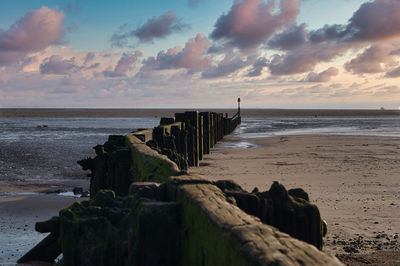 Wooden posts on beach against sky during sunset