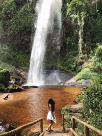 Side view of woman standing against waterfall