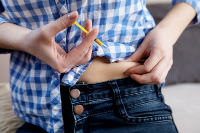 Midsection of woman injecting syringe on her stomach