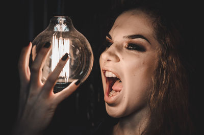 Portrait of woman holding glass while standing against black background