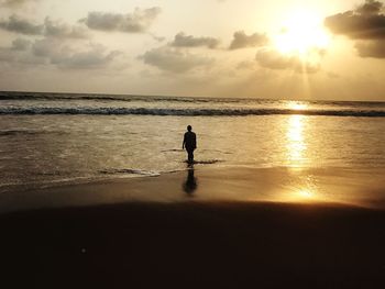 Silhouette woman walking on shore at beach against sky