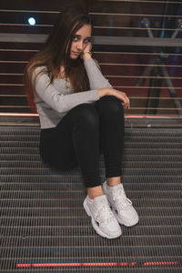 Full length portrait of young woman sitting on footbridge