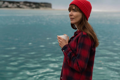 Beautiful woman with coffee cup standing by lake