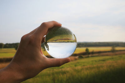 Cropped hand holding crystal ball on landscape