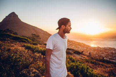 Young man standing on land against sky during sunset