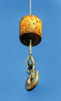 Rusty hook of crane against clear blue sky