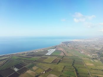 Aerial view of agricultural field by sea against sky