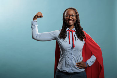 Portrait of young woman with arms crossed standing against blue background