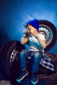 Boy in a white t shirt shirt and hat sits on a background of car wheels on a blue