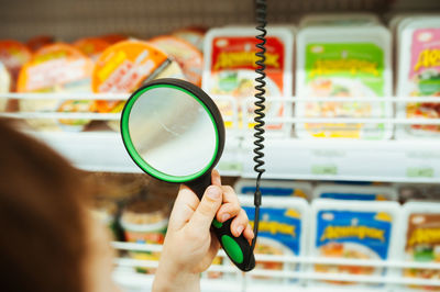 People holds magnifying glass in hand in store and looks at price of product through glass