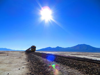 Sun shining over mountain range and a train coming against clear blue sky