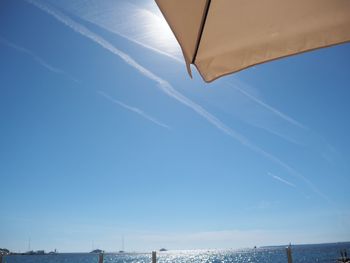 Low angle view of vapor trails over sea against blue sky