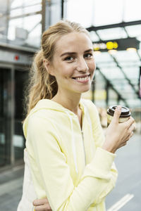Portrait of cheerful woman holding disposable coffee cup at railroad station