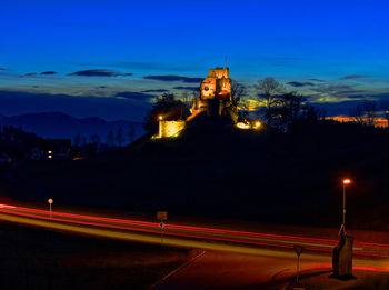 Light trails on road by building against sky at night