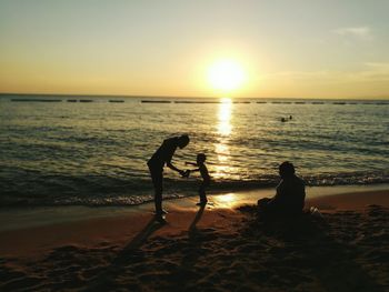 Silhouette people on beach against sky during sunset