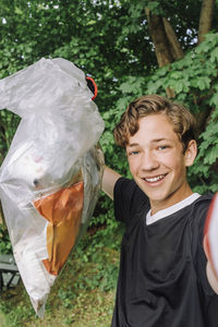 Portrait of happy teenage boy showing garbage bag with plastic