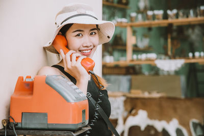 Portrait of a smiling young woman talking on payphone