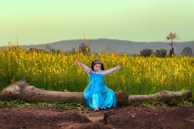 Portrait of girl in costume sitting on log against sky