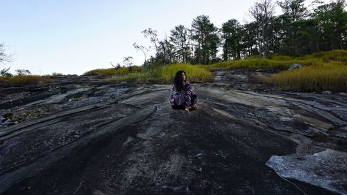 Woman sitting on dirt road against sky