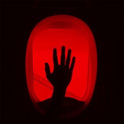 Close-up of silhouette hand on illuminated red light