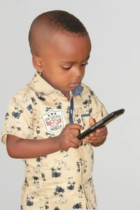 Cute boy holding mobile phone while standing against wall