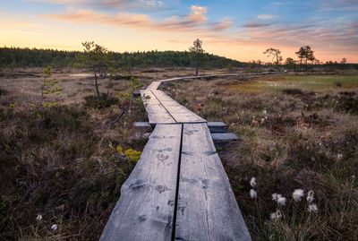 Boardwalk on landscape against sky during sunset