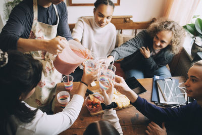 High angle view of teenage boy serving smoothie to friends in glasses at home