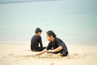 Siblings playing with sand at beach