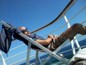 Low angle view of men sitting on deck chair in boat against blue sky