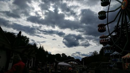 Silhouette people at amusement park against cloudy sky