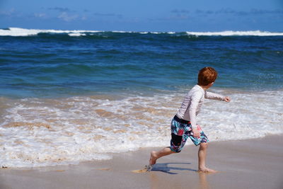 Young boy running from the waves on the beach in hawaii. 