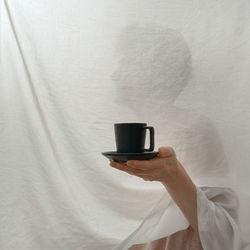 Abstract woman hiding behind white curtains holding a cup of coffee