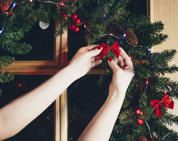 Cropped hands of woman hanging decorations on christmas tree