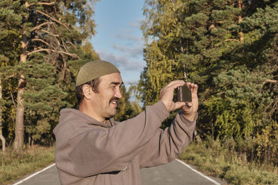 Portrait of man photographing with mobile phone in park