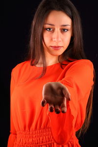 Portrait of woman in red dress gesturing against black background