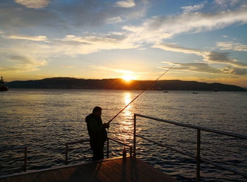 Silhouette man fishing in sea against sunset sky