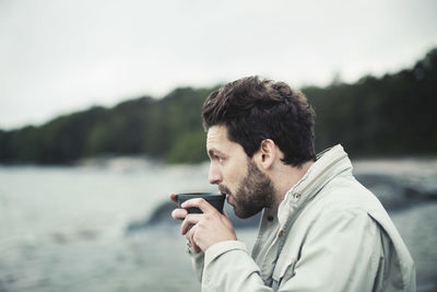 Side view of man drinking coffee at sea shore