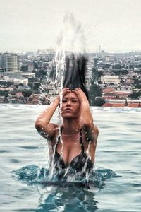 Sensuous woman tossing hair in infinity pool against cityscape