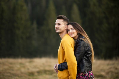 Portrait of woman embracing boyfriend while standing against trees