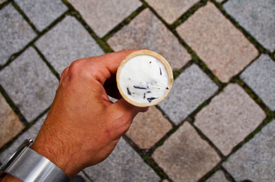 Cropped image of hand holding ice cream cone on paved footpath