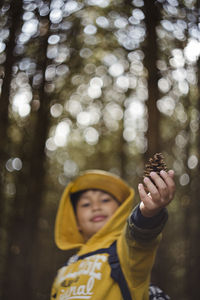 Portrait of smiling boy holding pine cone in forest