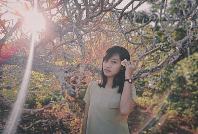 Portrait of young woman standing by tree