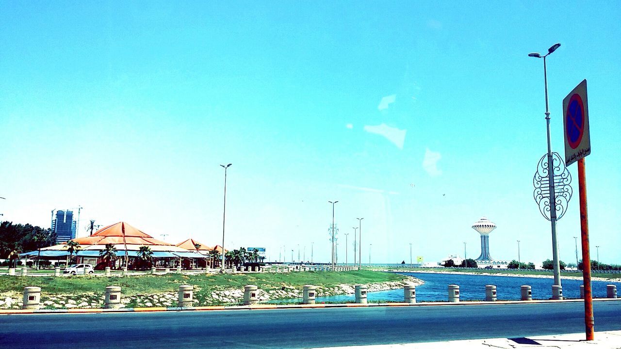 street light, blue, clear sky, building exterior, built structure, architecture, sky, transportation, lighting equipment, copy space, tree, lamp post, sunlight, road, outdoors, street, day, no people, city, mode of transport