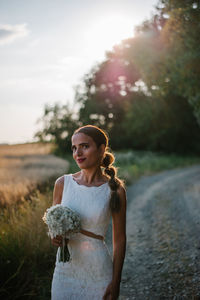 Portrait of bride standing on dirt road against sky