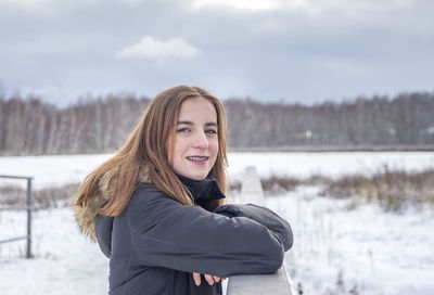 Portrait of smiling young woman standing against lake during winter