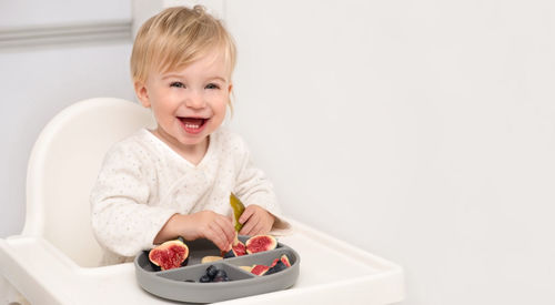 Laughing caucasian blonde toddler about 1-2 year old,eating from silicone plate fresh fruits