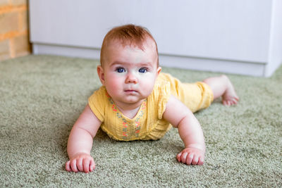 Portrait of little caucasian baby girl in yellow dress. child trying to crawl on a floor.