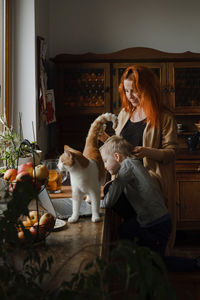 Ginger haired woman on kitchen with child and cat looking in laptop. vintage house, cozy family life